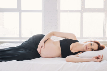 Obraz premium Pregnant woman lying on the white sheet thoughtfully