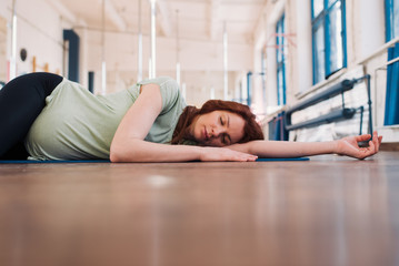 Fototapeta na wymiar Pregnant woman lying on the floor with eyes closed in a fitness room