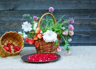 Fototapeta na wymiar клубника в тарелке и земляника в корзине лежат рядом с корзиной полевых цветов