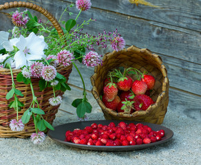 плетеная корзина стоит с полевыми цветами ис  тарелкой  ягод земляники