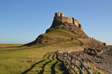 An iconic view of Lindisfarne (Holy island) with the castle on its distinctive  hill against a blue sky 