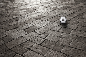 The sunset on old cobblestone with soccer ball on the floor. Conceptual danger urban football field...
