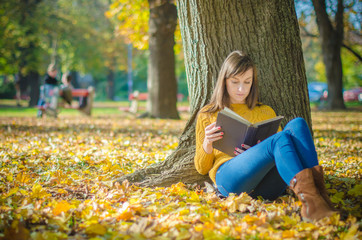 Pretty woman sitting and reading book in the autumn park