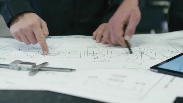 Close-up of two engineers discussing a blueprint in a factory. Shot on RED Cinema Camera.
