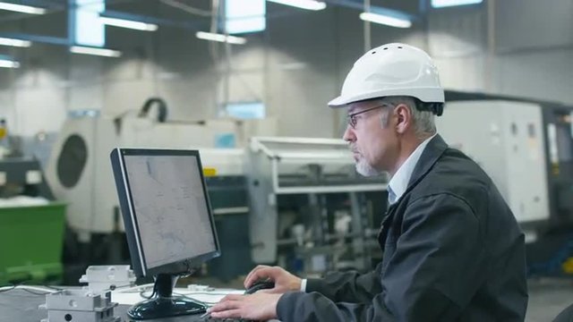 Senior engineer in glasses is working on a desktop computer in a factory. Shot on RED Cinema Camera.