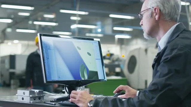 Senior engineer in glasses is working on a desktop computer in a factory. Shot on RED Cinema Camera.