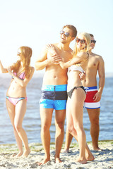 Happy couple and their playful friends relaxing at the beach, outdoors