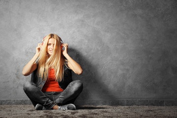 Young woman sitting on the floor and listening to music on a grey wall background