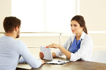 Doctor talking to male patient in room on light background