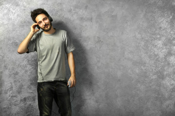Young bearded man listening music with headphones on grey wall background