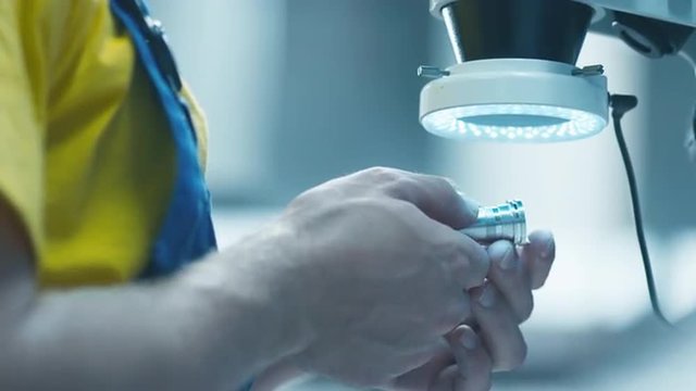 Engineer in a factory is inspecting a metal detail under a microscope with flashlight. Shot on RED Cinema Camera.