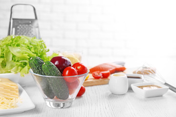 Kitchen utensils and ingredients for salad on table, on light background