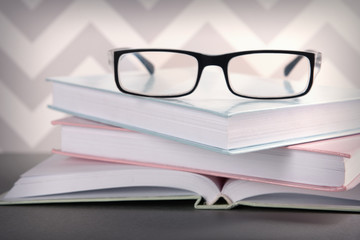 Books and eyeglasses on grey table against ornament wall, close up