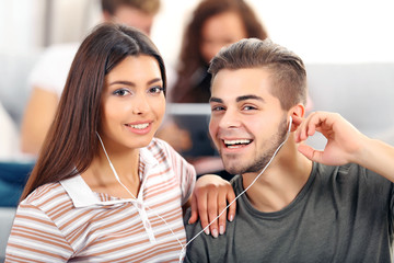 Teenager couple listening to music with earphones in living room