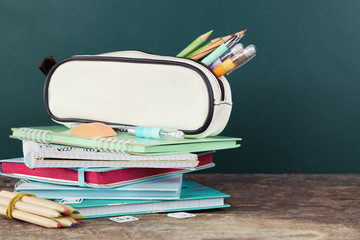 Pencil case with various stationery on old  wooden table, on blackboard background