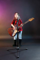 Fototapeta premium Beautiful little girl with microphone and guitar on dark purple background