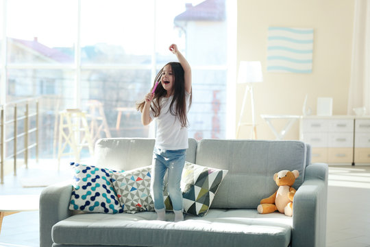 Beautiful little girl singing in a pink hairbrush and has fun in the room