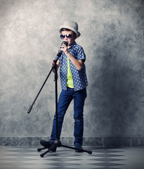 Little boy singing with microphone on a grey wall background