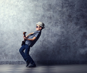 Fototapeta na wymiar Little boy playing guitar on a grey wall background