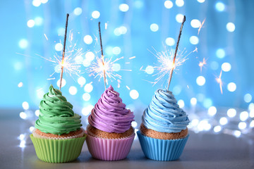 Varicolored cupcakes icing with sparklers in a row on a glitter background