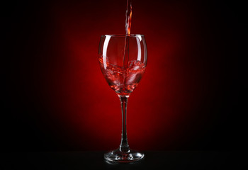 Wine pouring in glass on dark red background