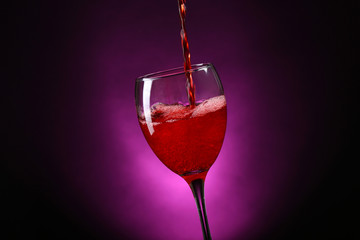 Wine pouring in glass on dark purple background