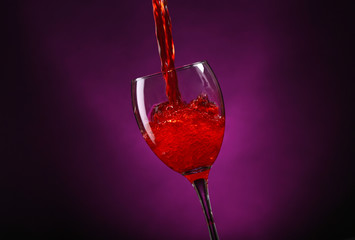 Wine pouring in glass on dark purple background