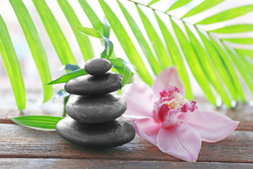 Obraz na płótnie Canvas Spa stones with palm leaves and pink orchid on wooden background