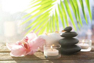 Fototapeta na wymiar Spa stones with towel, candles, palm leaves and pink orchid on wooden background