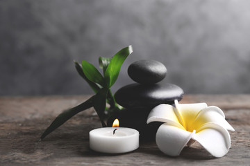 Spa stones with candle, bamboo and tropical flower on wooden table against grey background