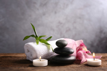 Obraz na płótnie Canvas Spa stones with pink orchid, candles, bamboo and towel on wooden table against grey background