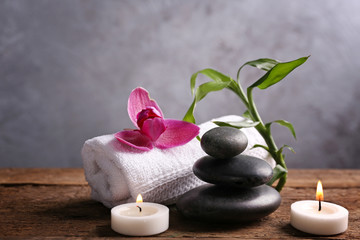 Fototapeta na wymiar Spa stones with candles, purple orchid, bamboo and towel on wooden table against grey background