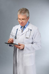 A handsome doctor with stethoscope and tablet standing on grey background