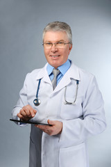 A handsome doctor with stethoscope and tablet standing on grey background
