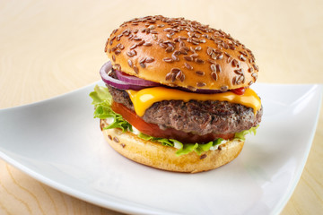 Burger with tomato , lettuce , mayonnaise , cheese , onion , ketchup and flax seeds on white dish