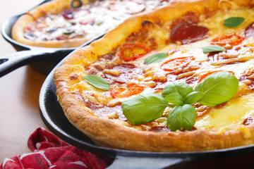 Cast iron skillet pan pizzas on wooden tabble closeup