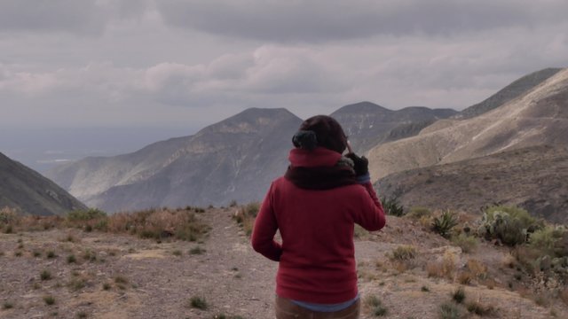 Woman using high tech google glasses near a cliff of a mountain in a windy day. 4k