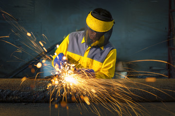 The worker grinding metal in manufacturing plant, sparks flying