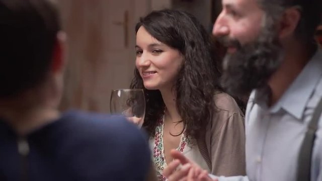 Young woman talking with her friends at dinner. She drinks wine and laughs. The camera moves. 4K, UHD