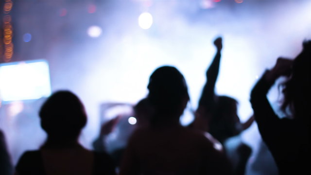  Blurred footage of crazy crowded party with people dancing on the dancefloor, waving their hands, feeling awesome. Attractive male and female silhouettes reveals in strobe light rays. 