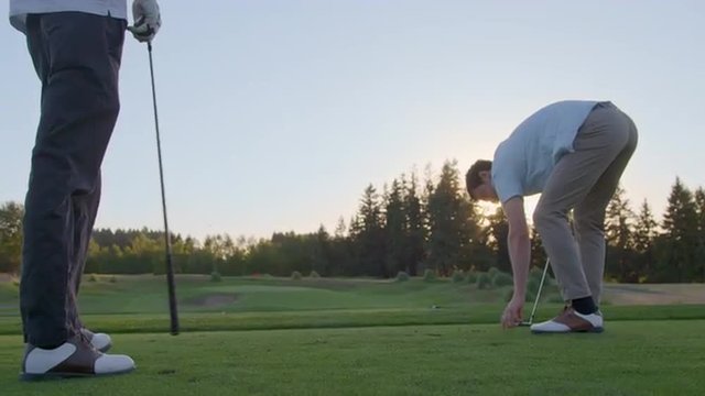 On the tee, a young man offers some tips to his friend, who takes a practice swing