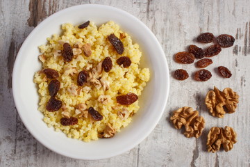 Cooked millet groats with raisins and walnuts on white plate, healthy food and nutrition