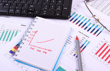Pen, glasses and computer keyboard on financial graph, business concept