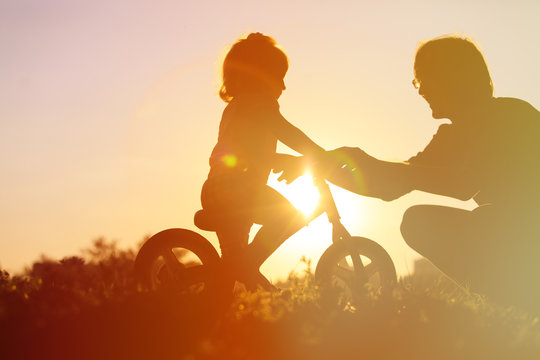 father teaching daughter to ride bike at sunset