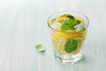 Soda water or mineral water with limes, lemons, ice and mint leaves on light blue background, can...