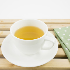 The cup of Japanese green tea and green cotton fabric on wooden tray.