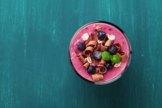 Healthy Breakfast Of Smoothie, Dessert, Yogurt Or Milkshake With Frozen Blueberry And Oats Decorated Grated Chocolate And Mint Leaves On Wooden Rustic Table, Top View