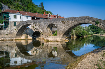 Fototapeta na wymiar Rijeka Crnojevica old bridge panoraic view with reflections on the calm river waters.