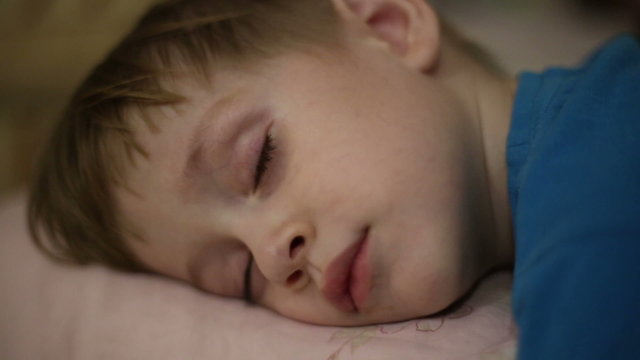 Little boy falls asleep, his eyelids heavy and eyes closed
