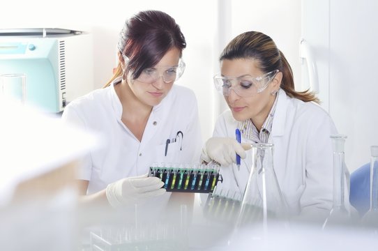 Attractive young PhD students scientists  observing the blue, yellow and green indicator color shift after the solution destillation in chemical laboratory 